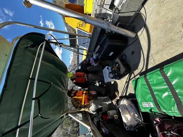 two male scientists look at computer on a boat next to yellow pontoon platform housing lake water profiler sensors