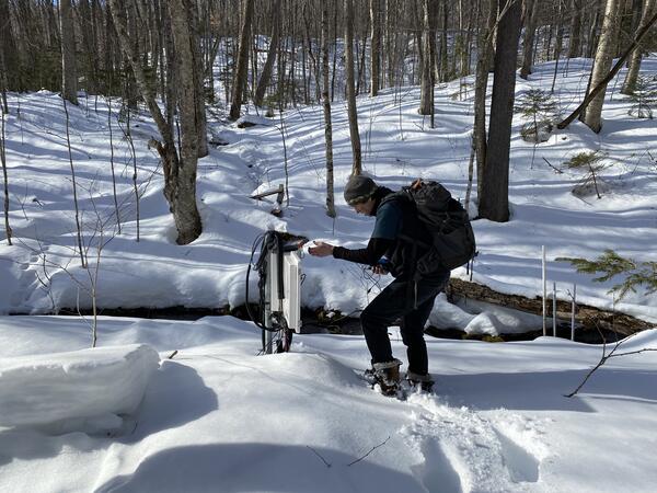 A man in the snowy woods looks at a data logger.