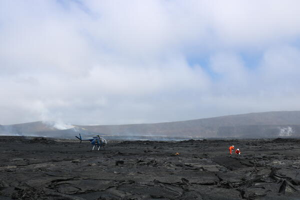 Color photograph of scientists working in volcanic crater with vent in background