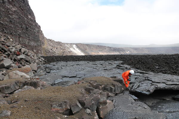 Color photograph of scientist collecting lava sample from crater floor