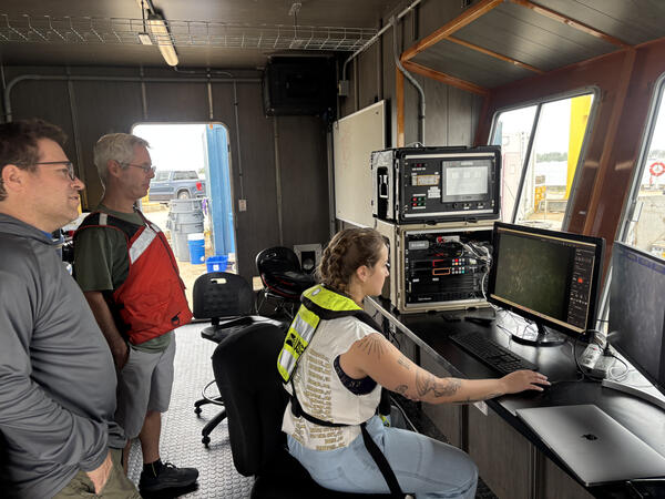 Three people staring at computer screens showing images of the seafloor