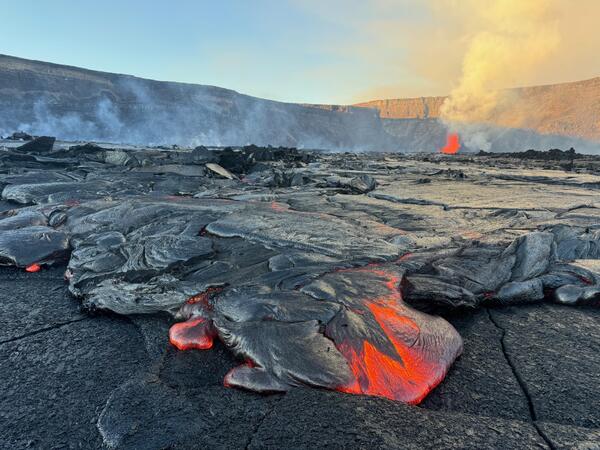 Color photograph of lava flows with erupting vent in the background
