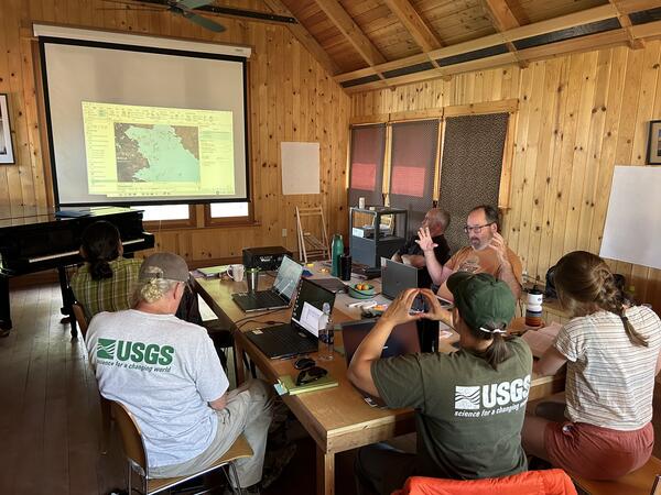 A group of seven researchers sits around a table in a wood-paneled room