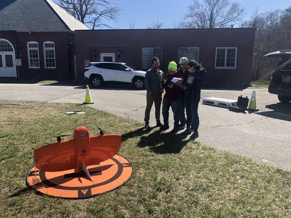 four people standing together looking at screen outside with drone on the ground