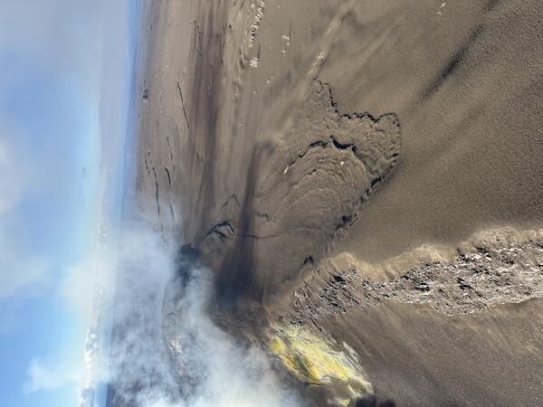 Color photograph showing volcanic gas wafting over a tephra-blanketed crater rim