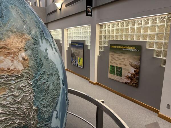 A portion of a large globe with scientific displays on a wall in the background