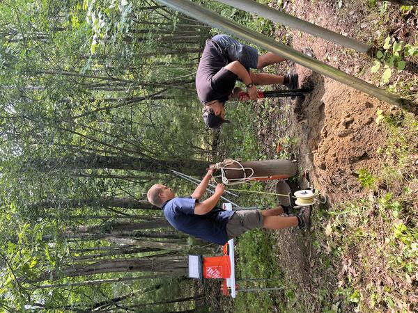 Two men install a groundwater well in the woods.