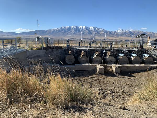 A concrete structure with seven large headgates that can divert water into a canal. The canal area is dry, and there are snowcapped mountains in the distance. 