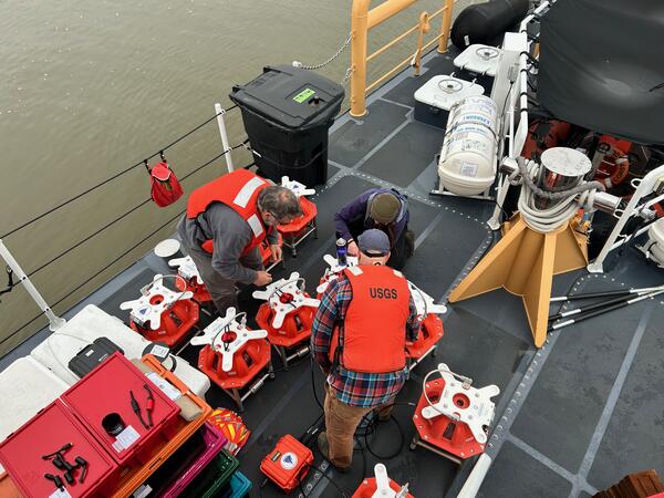 Three people on ship working on multiple pieces of equipment