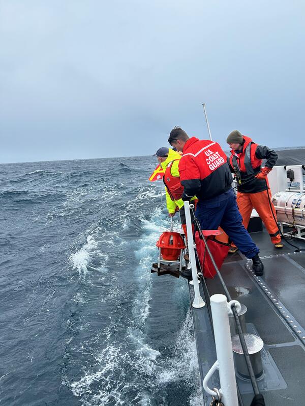 People leaning over side of ship lowering equipment into the water