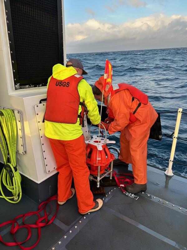 Two people on ship on the ocean hunched over equipment