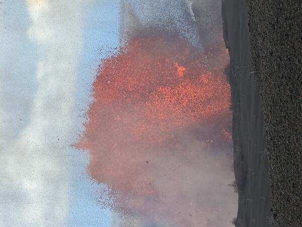 Color photograph of lava fountain during the day time with crater rim in the foreground