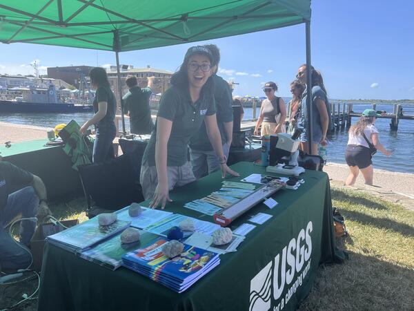 person standing behind USGS booth outside under tent