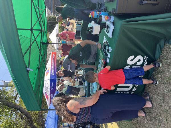 person behind USGS booth talking to adult and child outside under a tent