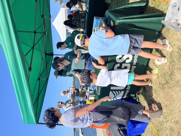 Person in USGS shirt talking to adult and two kids at USGS booth outside
