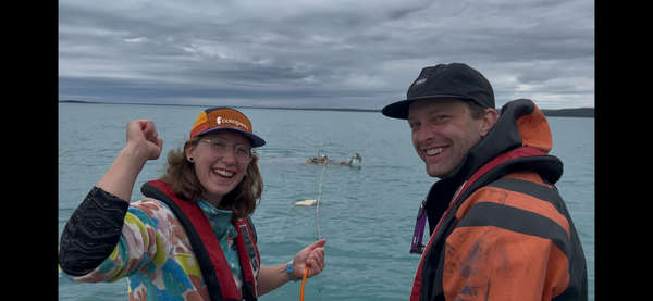 two people smiling, equipment in the water behind them