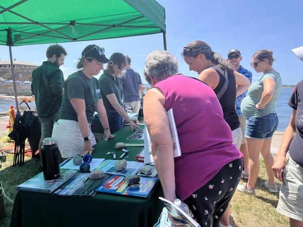 People in USGS shirts behind booth outside under tent talking to visitors