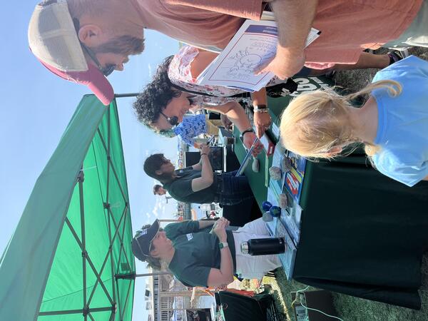 people taking handouts from USGS booth under tent outside on sunny day
