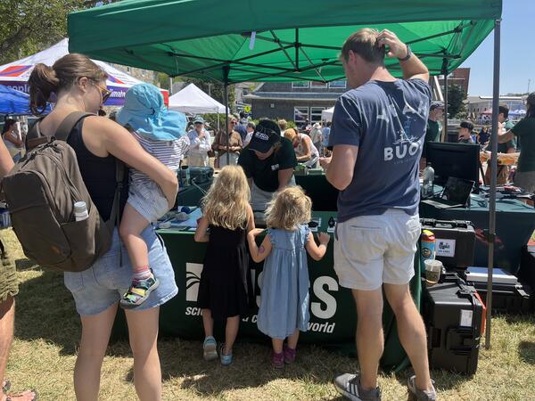a family with three kids visiting the USGS booth outside under a green tent