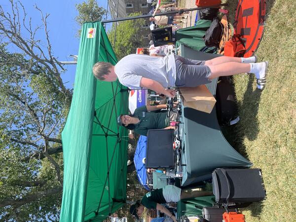 USGS scientist at booth outside with drones on it under tent outside talking to a person