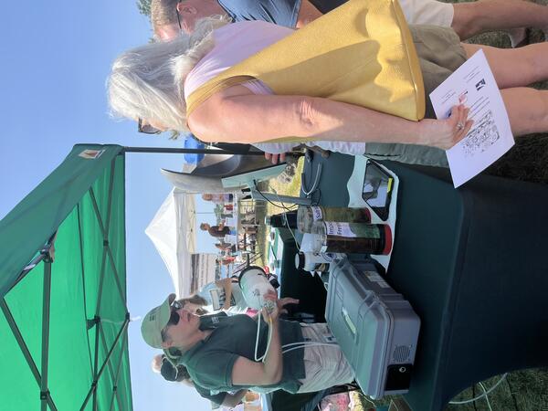 person showing equipment to visitor at USGS booth under tent outside