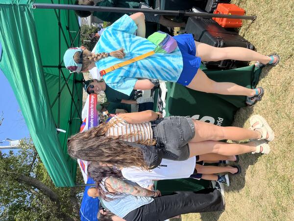people visiting USGS booth outside under tent on a sunny day