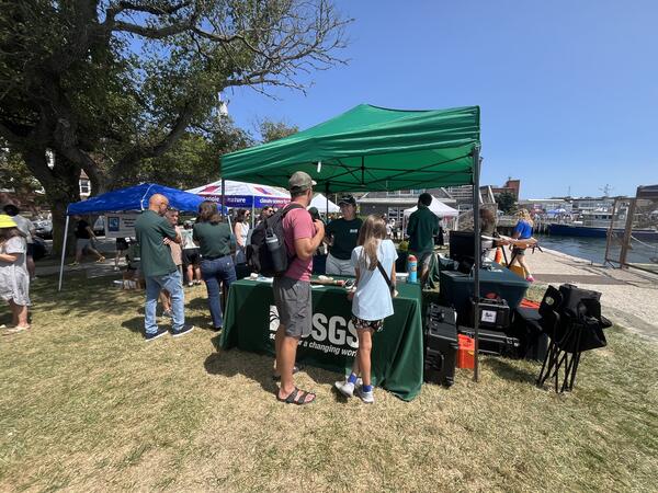USGS booth under tent outside by the ocean, people talking to USGS at the booth