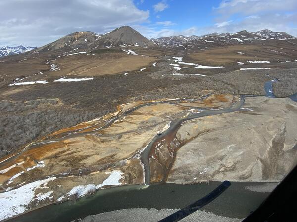 Orange river on a brown landscape and snowy mountains in the background.