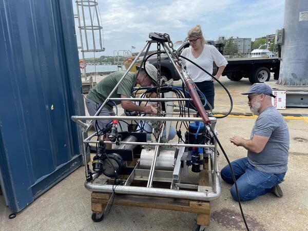 Three people working on a big instrument on a dock