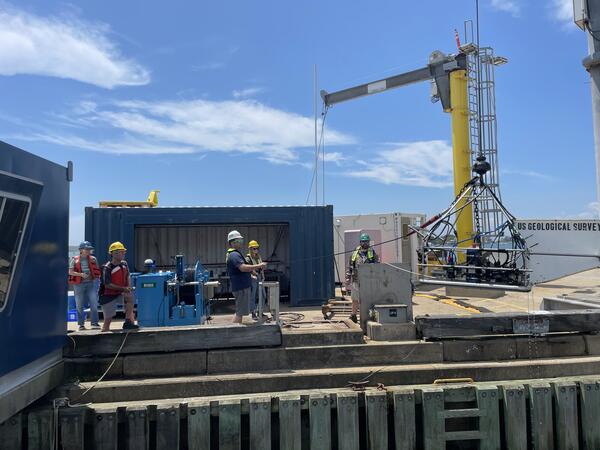 People on dock lowering large piece of equipment into the water