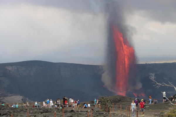 Lava fountains in the background with visitors visible in the foreground