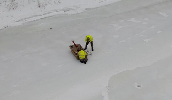 Two scientists collecting data by lowering a probe down through a hole cut in the ice