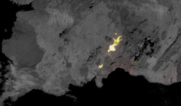 A thermal satellite image of an area of an erupting volcano that shines yellow to white on a gray landscape