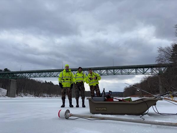 Three Scientists Standing on the Delaware River with their Ice Measurement Equipment in front of them