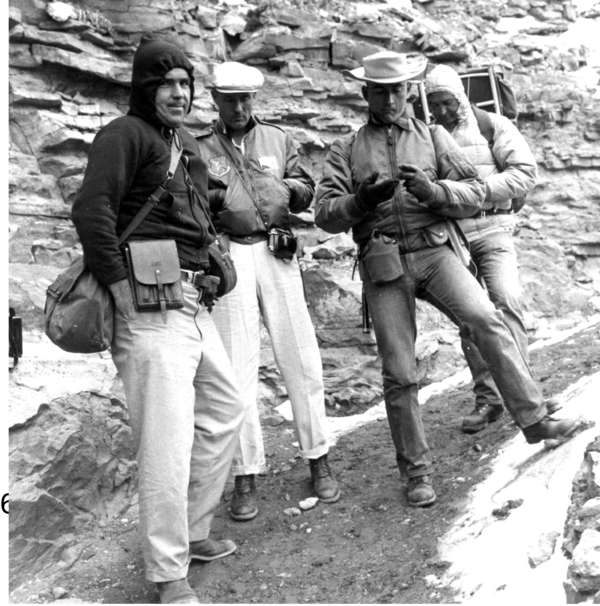 Four men in cold gear standing in front of a rock outcrop