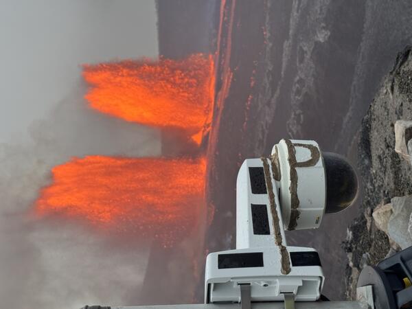Color photograph of webcam in the foreground and lava fountains in the background