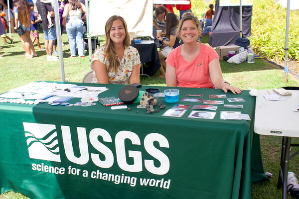 Two women sit at a USGS booth table at an outdoor event. 