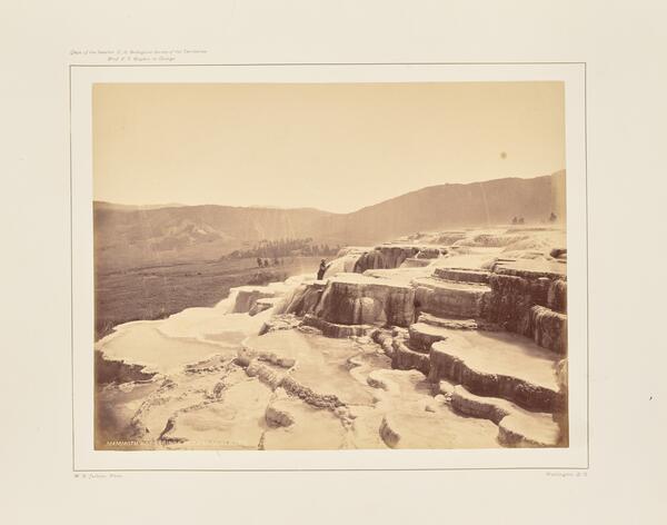 Sepia-toned photo of a man standing on a barren terraced hot spring formation
