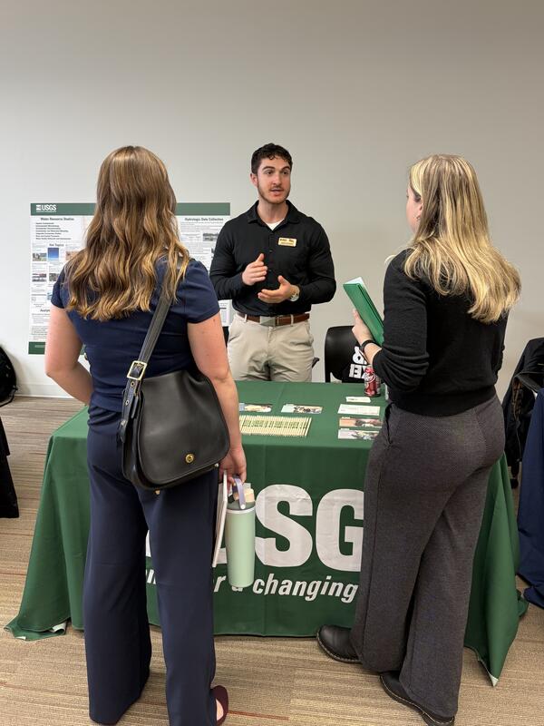 Man standing behind USGS table speaking to two women at a career fair