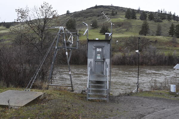 narrow rectangular metal gage house next to the river on a cloudy day.