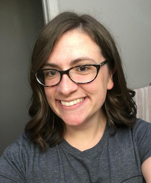 Person with long brown hair wearing glasses and smiling.