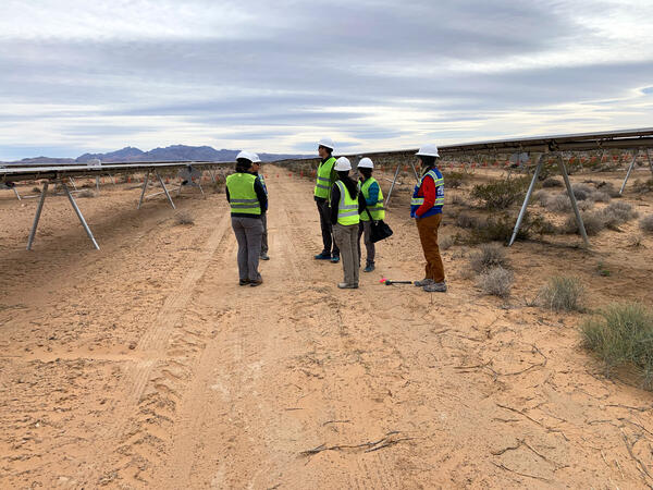 A group of people with safety vests stand between solar panels at the Gemini Solar Array in Nevada