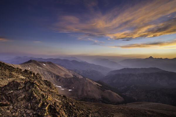 Barren and rocky mountainsides at sunset with some clouds in the distance