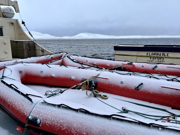 Red inflatable rafts with snow on top. Rafts on ship with snow covered mountains and sea in background.  