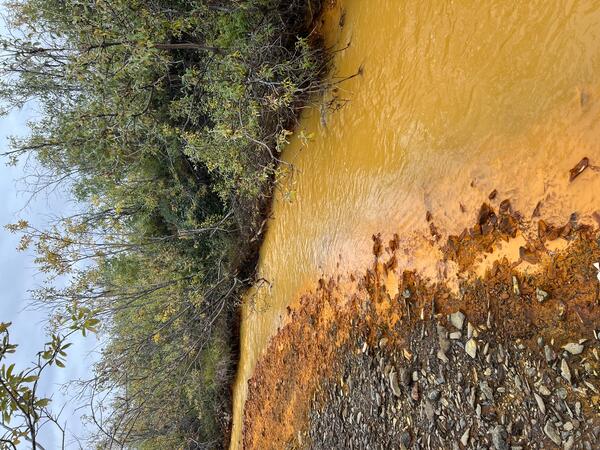 A pale orange river and dark orange deposits on river bank.
