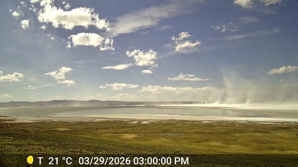 White dust blows off of shallow lake surface on a mostly sunny day