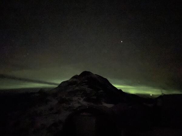 Dark mountain with green aurora behind.