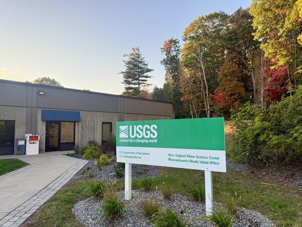 USGS Massachusetts office with a sign out front and trees in the back.