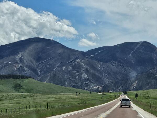 gray hill slopes in background lack vegetation highway and vegetation in image foreground