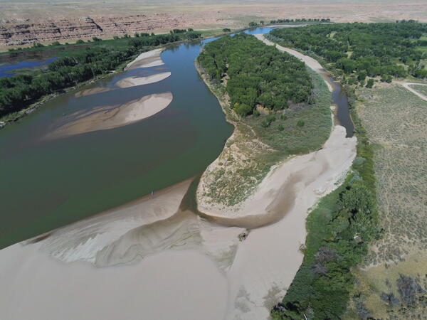 a blue-green river with many sand bars and beaches surrounded by trees and rock formations